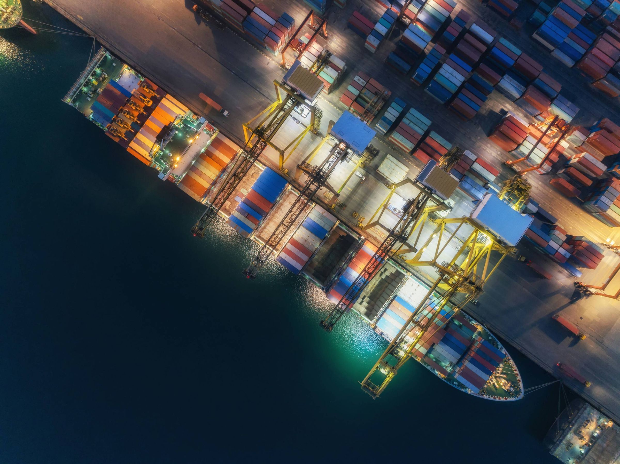 Aerial night view of a container ship being loaded at a brightly lit port