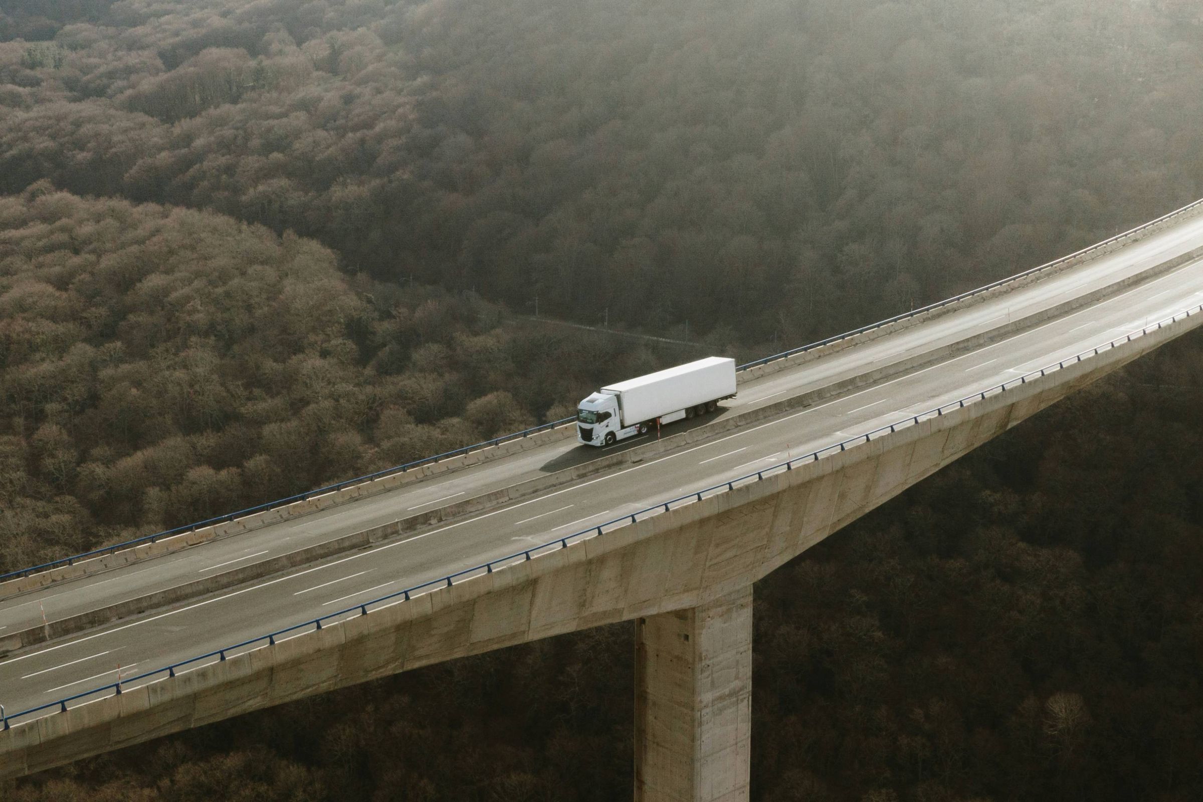 A white truck crossing a high bridge over a forested valley